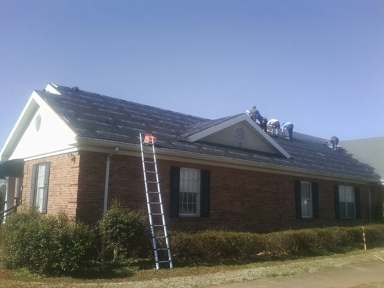 Crew tearing shingles off a brick ranch roof with a ladder set — Metal Roof Repair work by our crew in Valley Springs