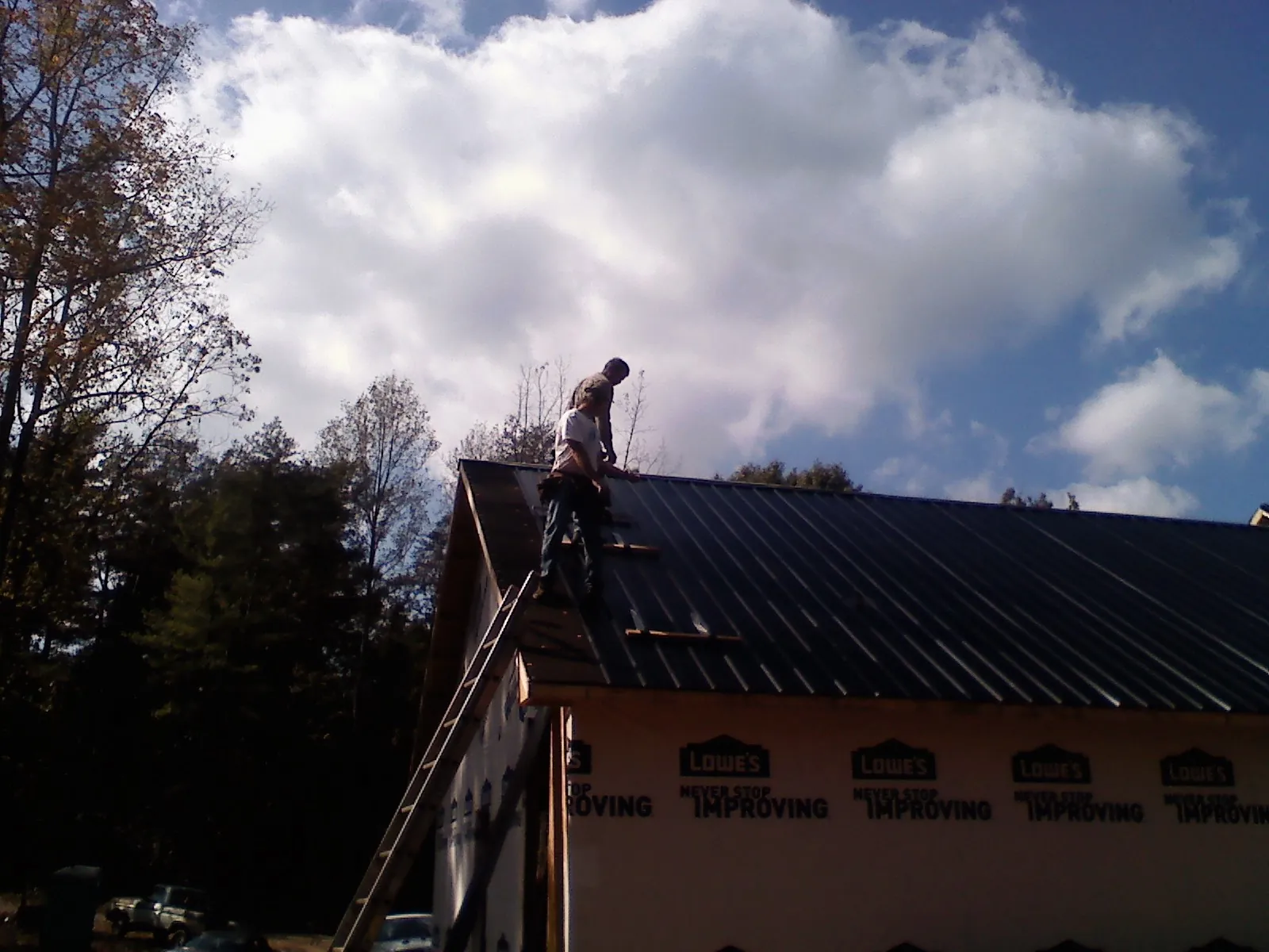 Roofer fastening dark metal panels high against a cloudy sky, from a Roof Inspection job in Valley Springs